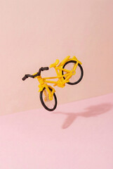 Miniature yellow toy bicycle floating in the air against a minimalist pink background.