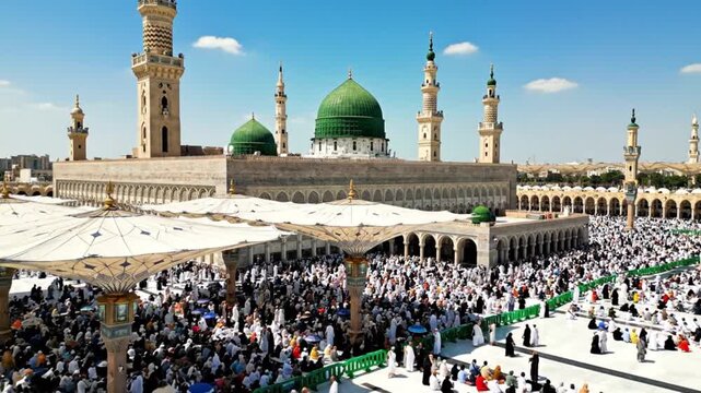 A grand complex features multiple green domes tall minarets and a large paved courtyard filled with many people under decorative sunshades on a bright day