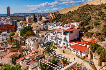 Mediterranean hillside neighborhood with colorful houses and city view, Elevated view of a Mediterranean hillside neighborhood with colorful houses, palm trees, terraces, and modern city skyline.