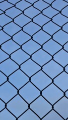 Fototapeta premium Close-up of a black chain link fence against a clear blue sky.
