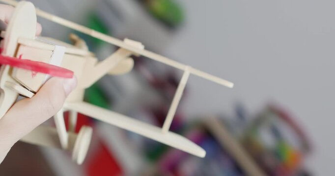 Little child plays with plywood biplane dreaming about flights in playroom closeup. Active kid has fun with vintage plane made of wooden constructor set at home POV