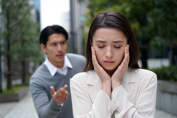 A woman covers her ears, appearing distressed, while a man gestures towards her, expressing frustration in a modern urban landscape. Generative AI.