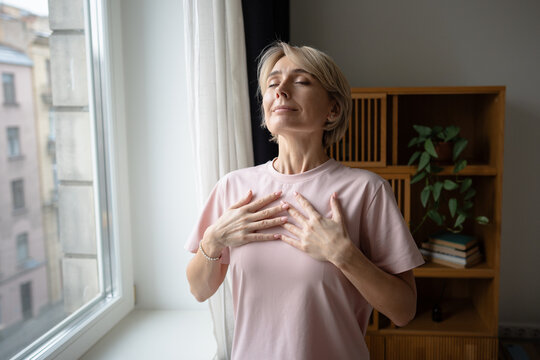 Relaxed confident woman in pajamas do daily breathing practice meditation for stress relief and relaxation. Positive smiling female practicing deep breath exercise, mental care everyday routine ritual