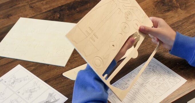 Child hands take part of vintage airplane model out of plywood sheet closeup. Smart kid plays with wooden development toy sitting at table. Construction set