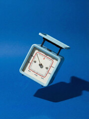 Floating vintage mechanical food scale on a bright blue backdrop. Creative concept for weight measurement and healthy lifestyle.