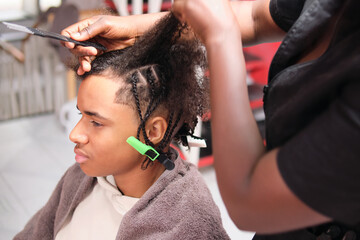Left-profile afro man with hairstylist sectioning hair for braids