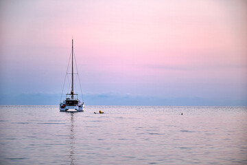 Fototapeta premium Sailboat in calm water during sunset with swimmer nearby enjoying the ocean