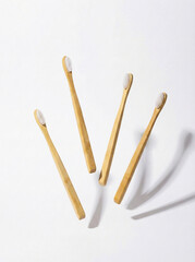Four eco-friendly bamboo toothbrushes with white bristles on white background.