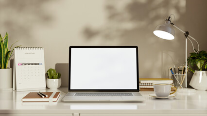 White screen laptop with calendar and coffee under lamp on table aside wall in living room or office
