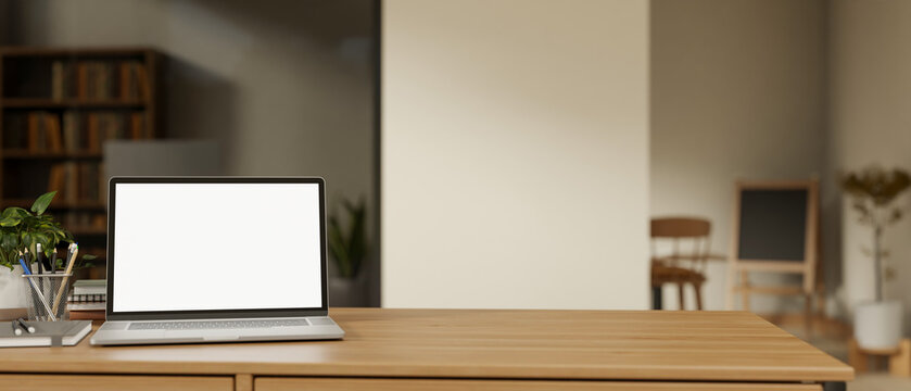 Blank screen laptop with book and pencil on wooden table across glass wall in a living room or cafe.