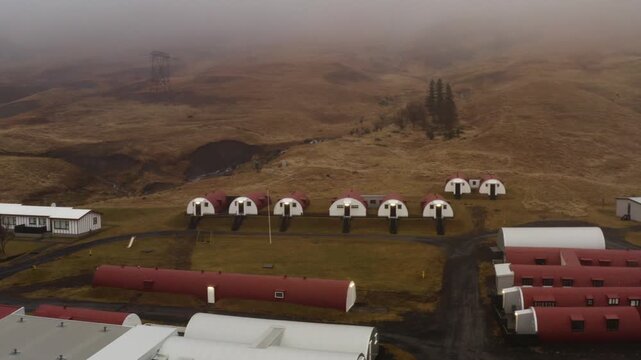 Drone view of Quonset huts on grassy land in Hvalfj&ouml;r&eth;ur Iceland under fog ww2