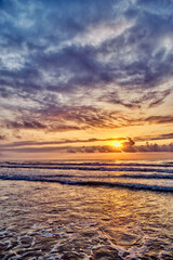 Fototapeta premium Sunset at the beach with waves and clouds over the ocean horizon in the evening