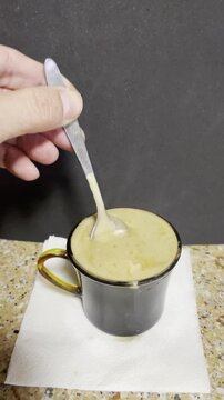 Taza de caf&eacute; caliente con espuma y mano dando vueltas y removiendo con cuchara