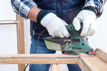 Craftsman. Adult carpenter using an electric sander to smooth an old wooden window. Construction industry, carpentry, housework do it yourself, workplace safety. Restoration.