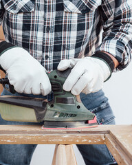 Craftsman. Adult carpenter using an electric sander to smooth an old wooden window. Construction industry, carpentry, housework do it yourself, workplace safety. Restoration.