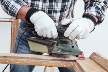 Craftsman. Adult carpenter using an electric sander to smooth an old wooden window. Construction industry, carpentry, housework do it yourself, workplace safety. Restoration.