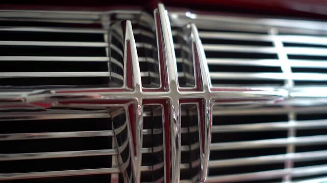 A close-up view showcases the polished chrome grill of a vintage automobile, with a central emblem and horizontal bars. The sleek, reflective surface