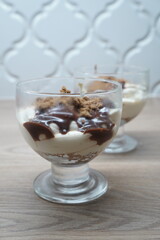 Delicious layered dessert in a glass with chocolate sauce and cookie crumbs