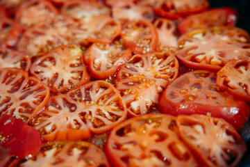 Sliced red tomatoes arranged in a pan, showing their juicy texture and seeds. Ideal for cooking or culinary backgrounds.