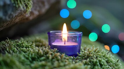 Softly glowing periwinkle votive candle flickering amidst mossy textures with blurred colorful bokeh lights