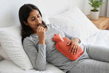 Woman in bed with hot water bottle and chocolate
