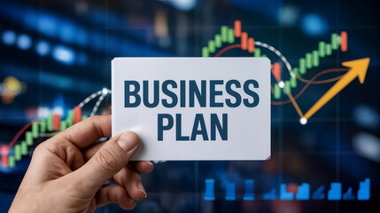Hand holding a card with the words business plan against a background of financial charts and graphs showing growth