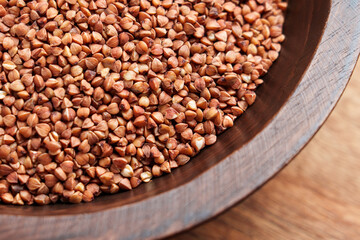 Raw buckwheat groats in wooden bowl. Natural grain texture of uncooked food ingredient. Healthy nutrition concept
