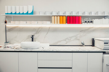 A clean and sterile cosmetology workspace featuring a marble countertop, various skincare products on shelves, and a sink for treatments.