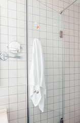 A modern bathroom with white ceramic tiles. A glass shower enclosure is visible, featuring a white towel hanging on a hook. Clean and minimalistic design.