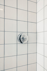 Ceramic bathroom tiles in a shower. The tiles are white with gray grout. A chrome shower control is mounted on the wall.