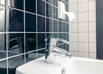 A modern bathroom with ceramic tiles. A modern bidet with a chrome faucet in a tiled bathroom. The wall has a mix of dark and light tiles, creating a stylish contrast.