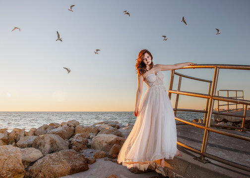 Young woman in a strapless gown standing on a beach with Flock of birds flying overhead