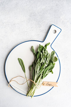 Overhead view of a bunch of fresh sage tied with string and a tag with the word sage on a chopping board