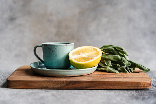 Close-up of fresh sage leaves on crockery on a  wooden chopping board with half a lemon and bunch of fresh sage