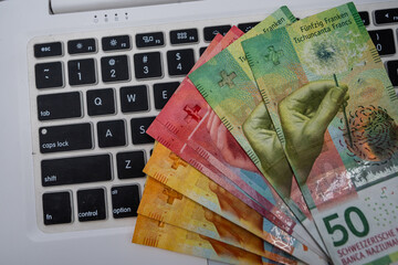 Swiss Franc banknotes near laptop on wooden surface illustrating budgeting, earnings and financial planning