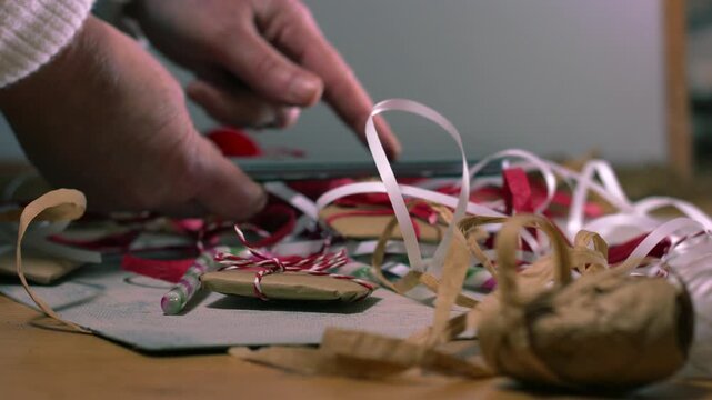 Christmas gift wrapped in string with hands using mobile phone in background