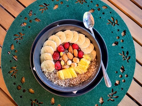 Overhead view of an Oatmeal bowl with banana slices, raspberries, pineapple and almonds on a table