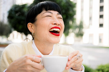 Smiling adult woman sitting outdoors in cafe enjoying drink and relaxing