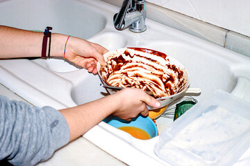 Child washing baking dish in home kitchen after cooking