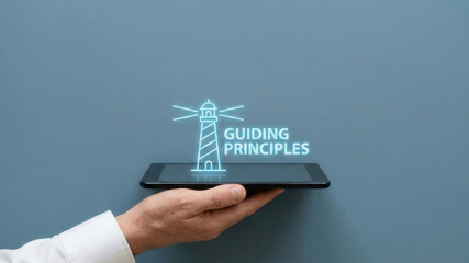 Business high level planning concept guiding principle lighthouse icon glows above digital tablet hand metaphor for corporate vision and leadership