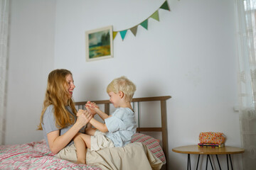 Mother and son enjoying playful moment on bed at home with joy
