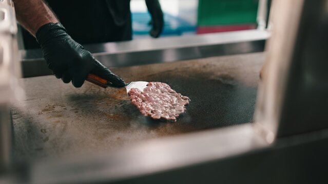 Chef in black gloves cooking a smash burger patty on a hot grill in a dark kitchen
