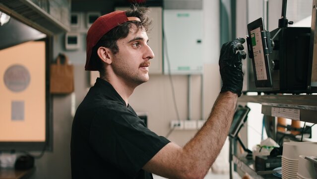 Chef working in dark kitchen, managing online delivery orders on tablet