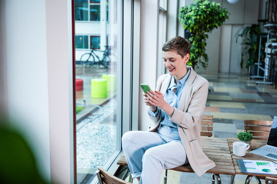 Businessperson sitting in modern office using smartphone and smiling