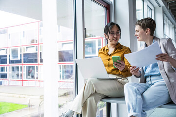 Coworkers discussing documents and using technology at modern office