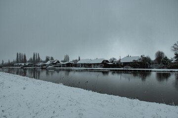 Dutch winter residential scene houses near water with snow while snowing as storm system brings unusually heavy snowfall in the Netherlands. Code Orange weather warning in effect. 