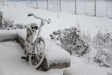 Dutch winter scene parked bicycle while snowing as storm system brings unusually heavy snowfall in the Netherlands. Code Orange weather warning in effect. Bike covered by layer of white snow