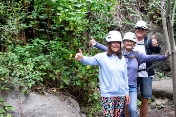 Happy seniors hikers with  protective helmets enjoying a trekking day on mountain looking at camera with thumbs up - Smiling tourists walking appreciating freedom, sport, healthy lifestyle in nature