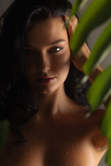 Fototapeta premium Nude Woman with Wet Skin Posing Behind Tropical Leaves