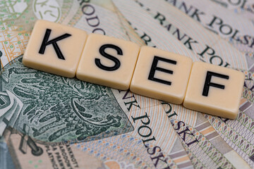 Blocks with the abbreviation KSEF, standing for National E-invoice System, are placed against a background of loosely spread Polish 100 PLN banknotes. The photo was taken under artificial lighting.